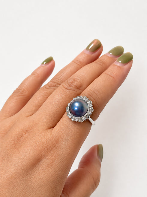 Ring with 12mm blue Mabe pearl and a halo of clear stones on a silver open-band setting.