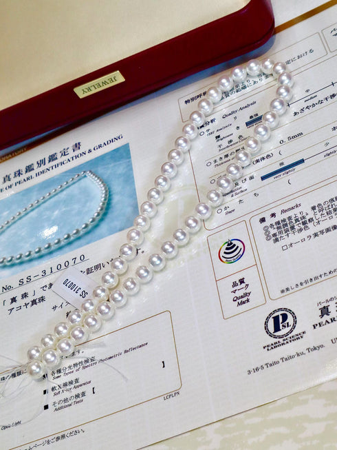 Pearl necklace with Hanadama Akoya white pearls on a red jewelry box beside a grading certificate
