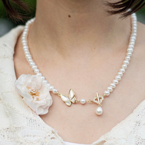 White freshwater pearl necklace with a gold-tone butterfly pendant and a dangling pearl drop