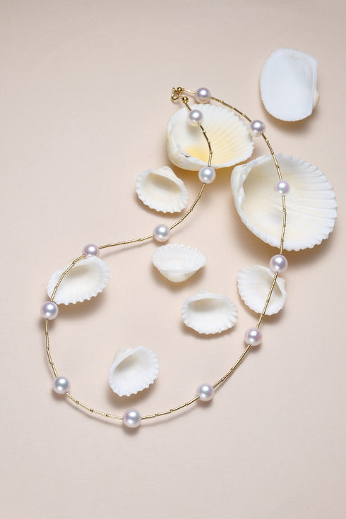 Necklace: 9 Akoya pearls on a gold tin-cup chain, 18K gold, displayed on beige background