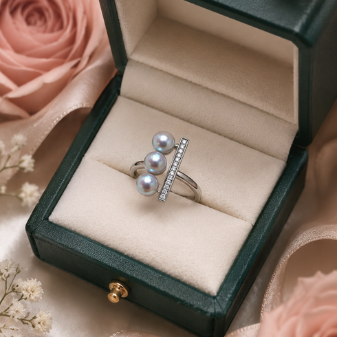Ring with three silver-blue Akoya pearls and a CZ-stone bar, open silver setting in a green jewelry box.