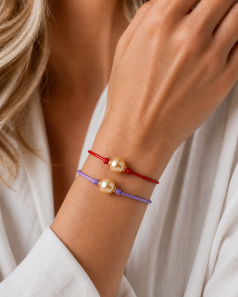 Bracelets: two knotted red and purple cord bracelets with golden South Sea baroque pearls