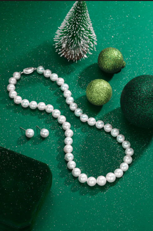 Graduated white freshwater pearl necklace with matching pearl studs on a green festive backdrop.