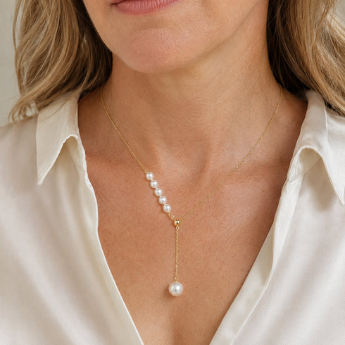 Y-shaped pearl pendant necklace on gold chain with a row of pearls and a dangling pearl drop.