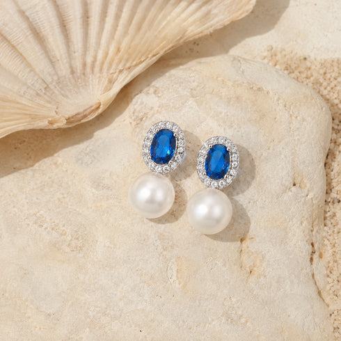 Earrings with blue oval CZ crystals halo and pearl drops, silver-tone setting.