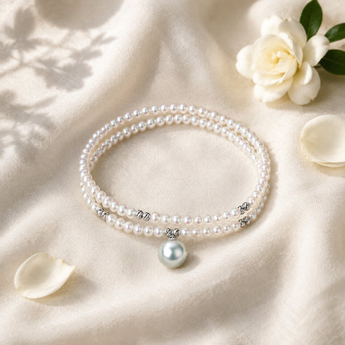 Double-strand Akoya pearl wrap bracelet with silver spacer beads and a blue pearl charm pendant.