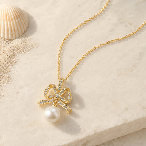 Pendant necklace featuring a gold bowknot with CZ crystals and a freshwater pearl drop