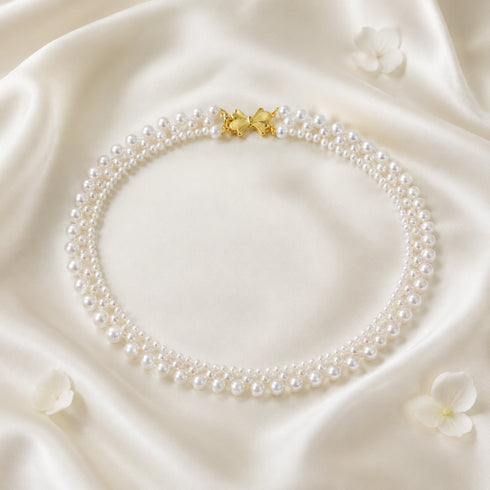 Gradual Pearl Braided Bow Necklace with white pearls and gold bow clasp on ivory satin backdrop