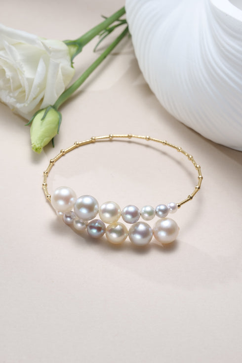 Bracelet: Celestial Tide Japanese Akoya Pearl Bangle in 18K gold with white and pastel pearls.